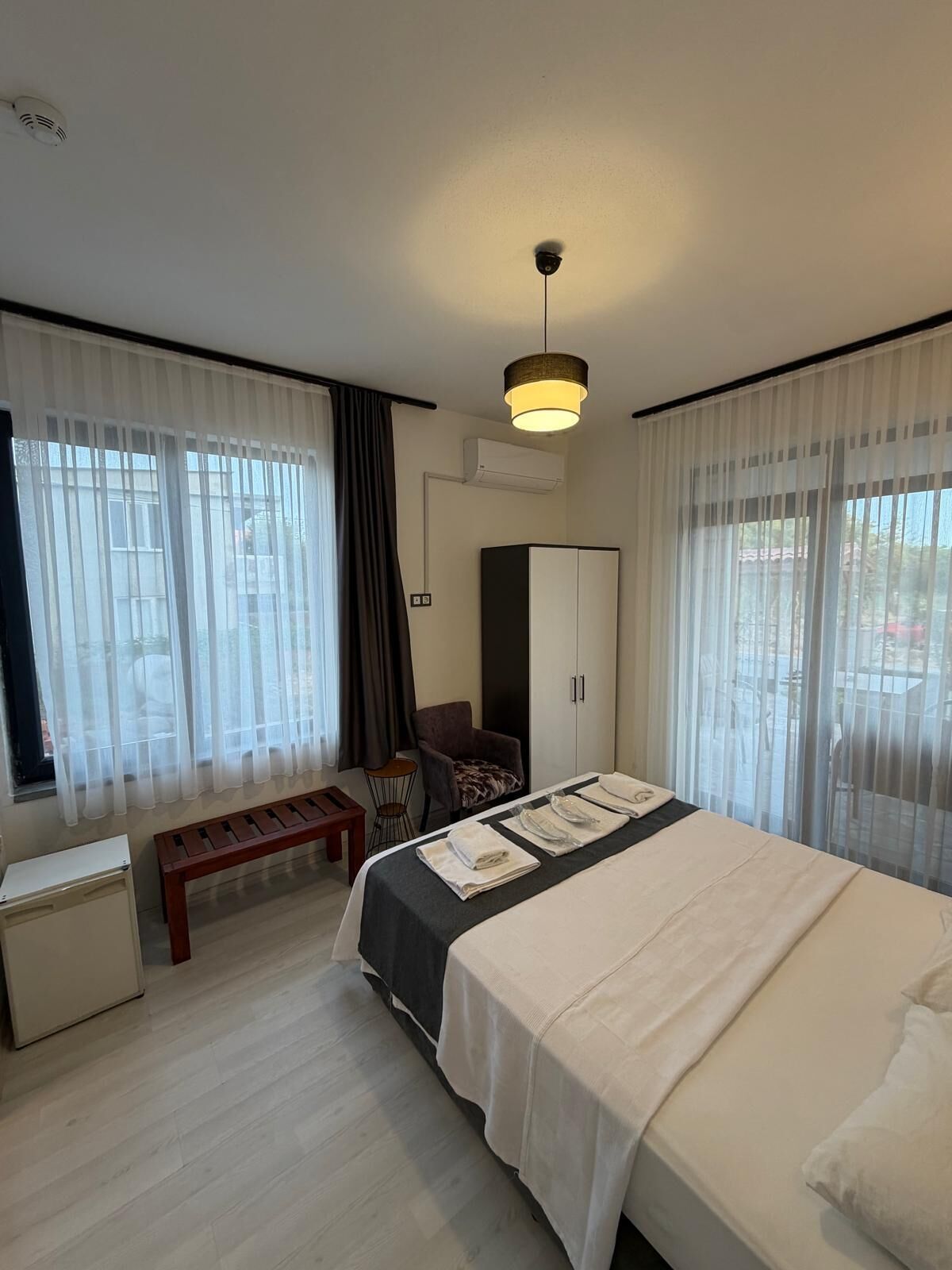 A hotel room with a bed, a desk, a chair, a bench, and a wardrobe.