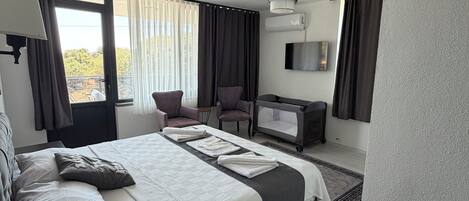 A hotel room with a large bed, a desk, a chair, a TV, and a window with curtains.