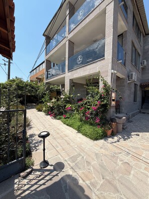 A multi-story building with balconies, a stone facade, and a garden with pink flowers. - Assos taş konak (Ayvacik)