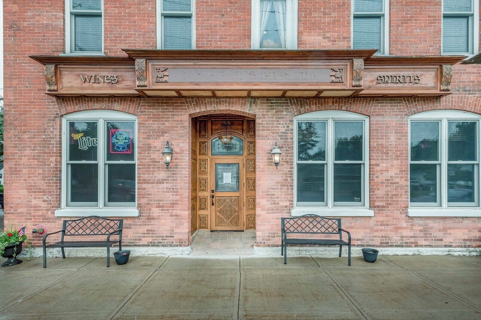 A brick building with a wooden front door, two benches, and signs for 'Wines' and 'Spirits'.