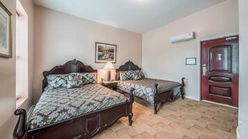 A bedroom with two beds, a nightstand, a lamp, a framed picture on the wall, and a door with a handle.