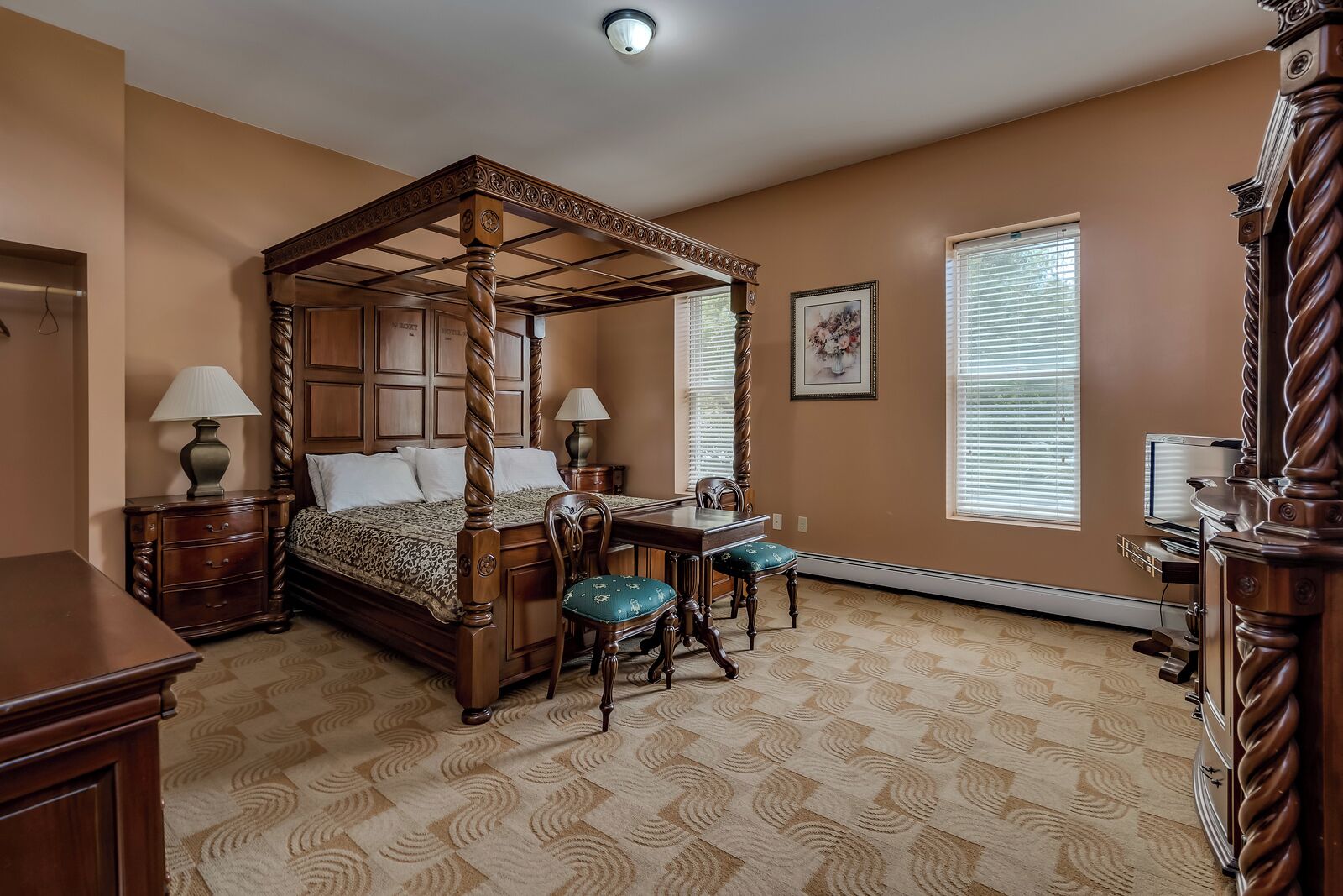 A four-poster bed with a wooden frame and a matching headboard, a dining table with chairs, and a small desk with a chair.