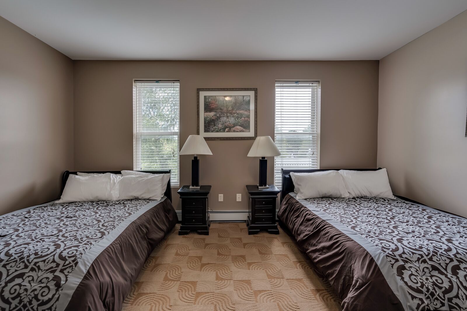 Une chambre avec deux lits, une table de chevet avec une lampe et un tableau encadré au mur.