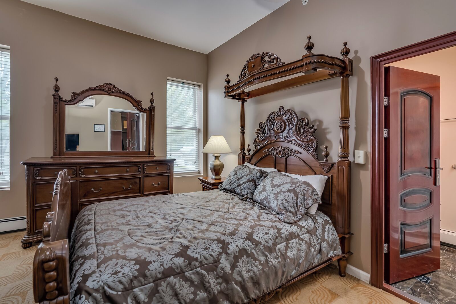 A bedroom with a large bed, a wooden dresser, a mirror, and a door.
