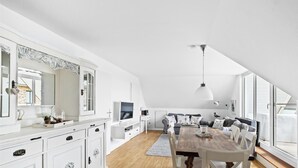 Tilava parvi- tai loft-tyyppinen asunto, jossa on korkea kattokorkeus, ruokailutila puupöydällä, valkoiset keittiökaapit ja suuri ikkuna, josta tulee runsaasti luonnonvaloa.