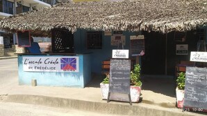 A small outdoor café with a thatched roof and a signboard displaying the menu.