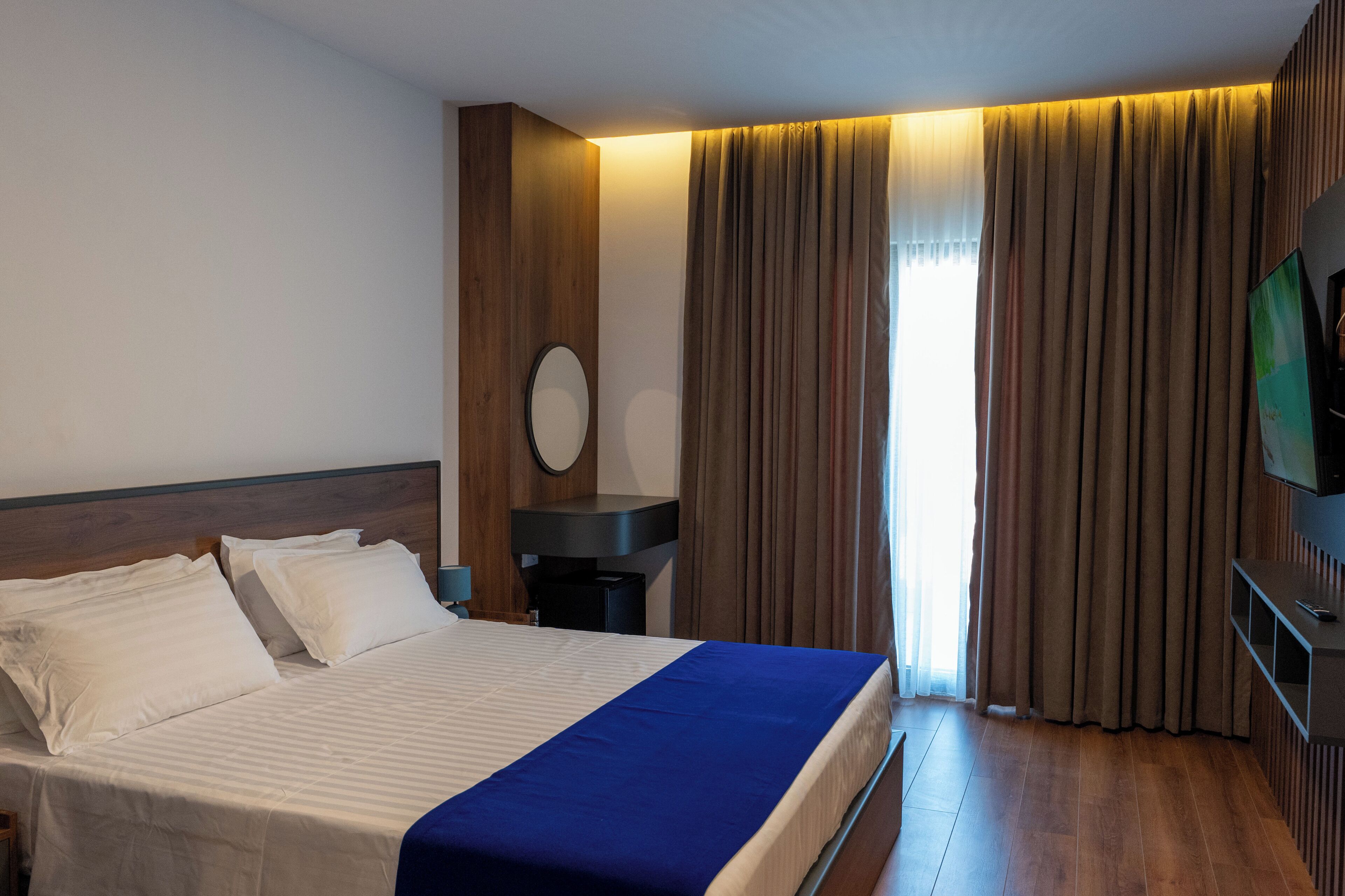 Une chambre d’hôtel avec un lit, une table de chevet, une télévision et des rideaux.