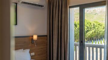 Hotellihuone, jossa on sänky, ilmastointilaite, yöpöytä lampun kanssa ja näkymä parvekkeelle, jossa on kaide.
