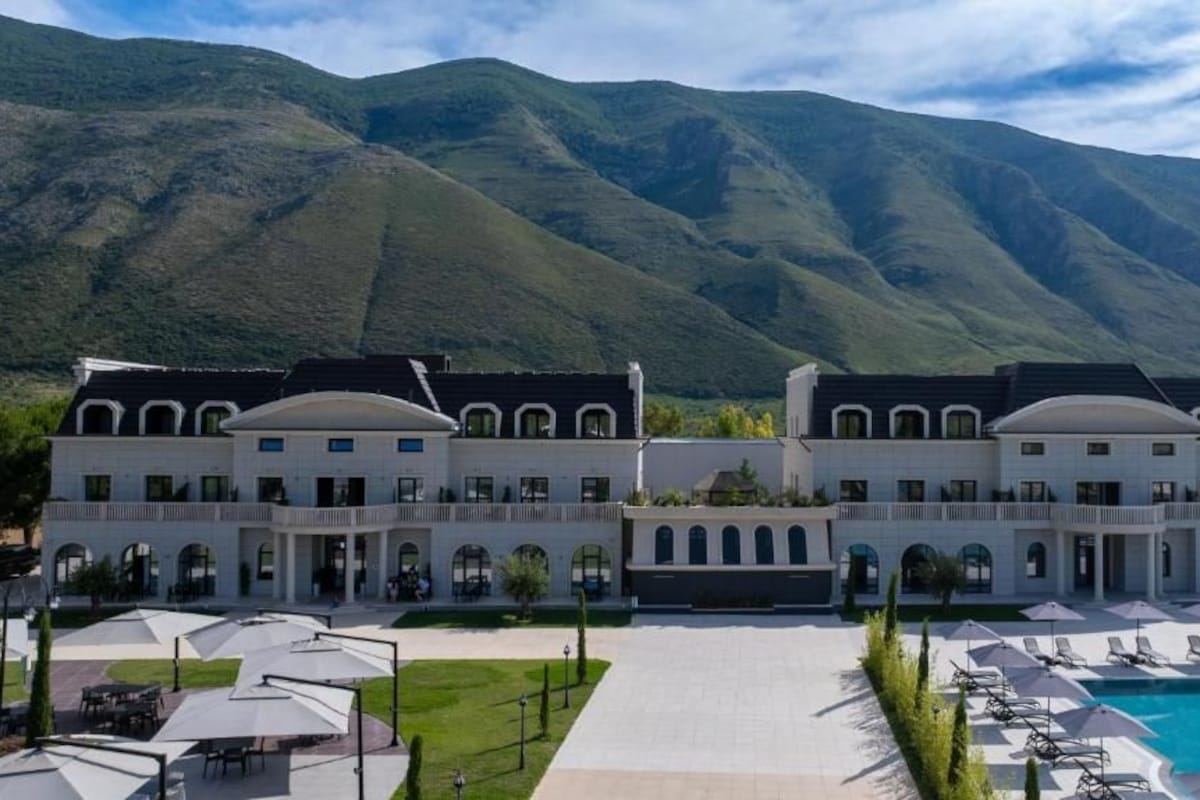 A large hotel with a central courtyard, a swimming pool, and mountain views.