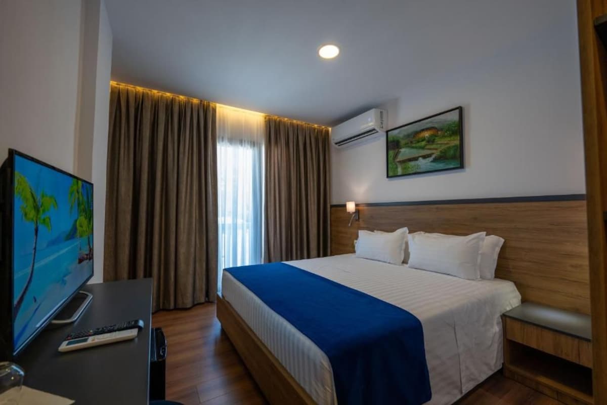 A hotel room with a bed, a TV, a desk, and a painting on the wall.