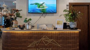 A reception desk with a television mounted above it, a wooden reception desk, and a potted plant to the right. - Acros Resort (Orikum)