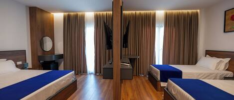 A hotel room with two single beds, a wooden floor, a large mirror, a TV, and a desk.