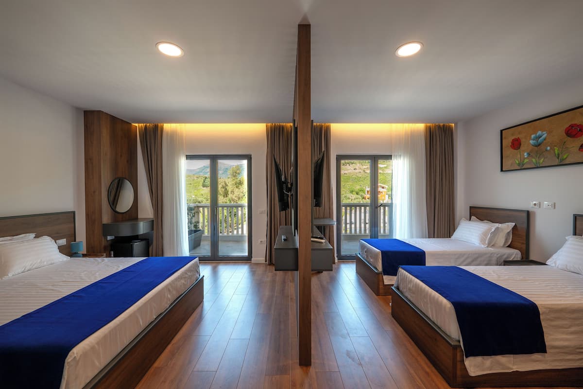 Habitación de hotel con dos camas, piso de madera, balcón con vistas y un cuadro en la pared.