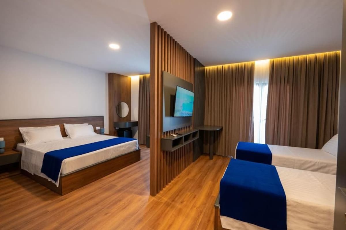 A hotel room with two beds, a TV, a wooden partition, and a small table.