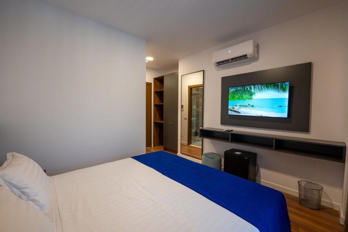A bedroom with a bed, a television mounted on the wall, and an air conditioning unit.