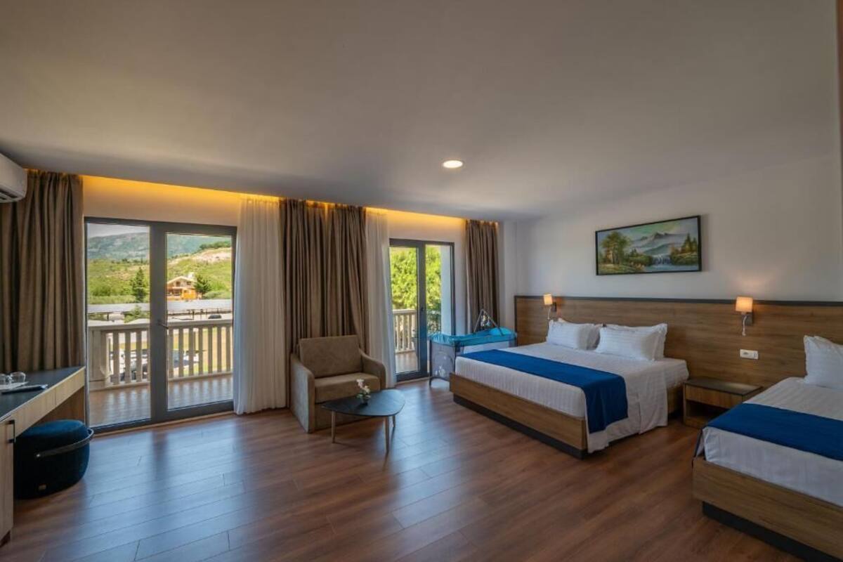 Habitación de hotel con dos camas, un escritorio, una silla y un balcón con vistas panorámicas.