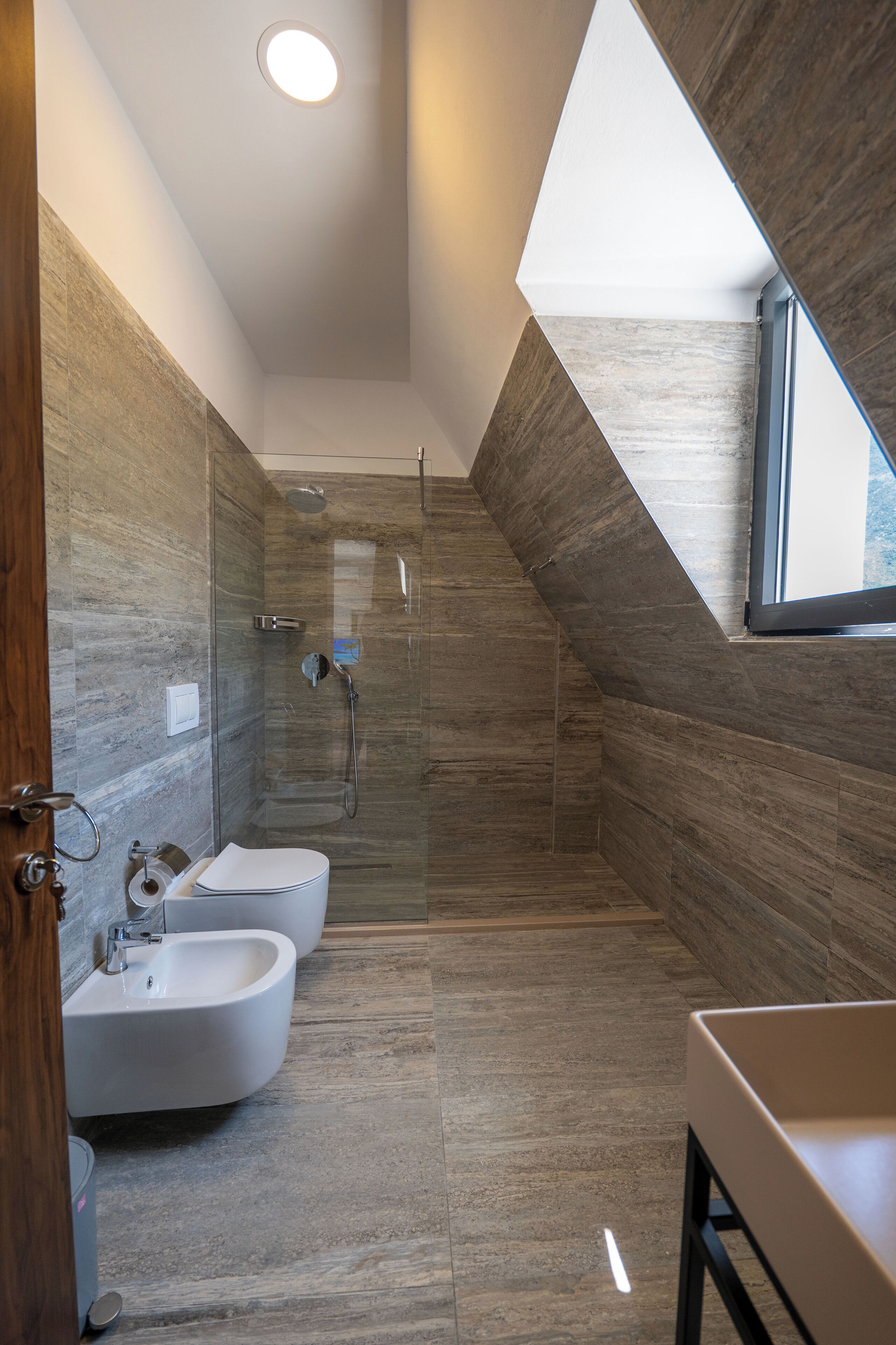 A modern bathroom with a shower, two sinks, and a window.