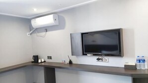 Habitació d'hotel moderna amb televisió de pantalla plana penjada a la paret, una cafetera i un dispensador d'aigua al taulell.