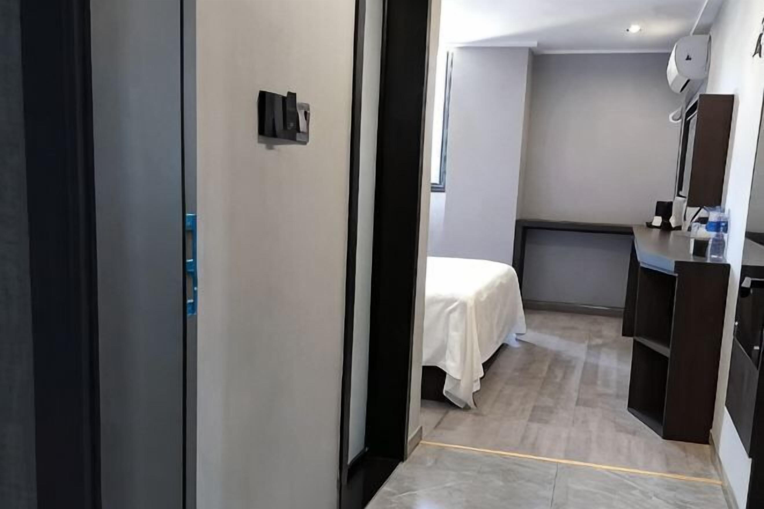 A hotel room with a bed, a desk, a mirror, and a small kitchenette.
