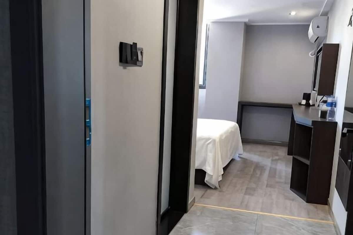 A hotel room with a bed, a desk, a mirror, and a small kitchenette.