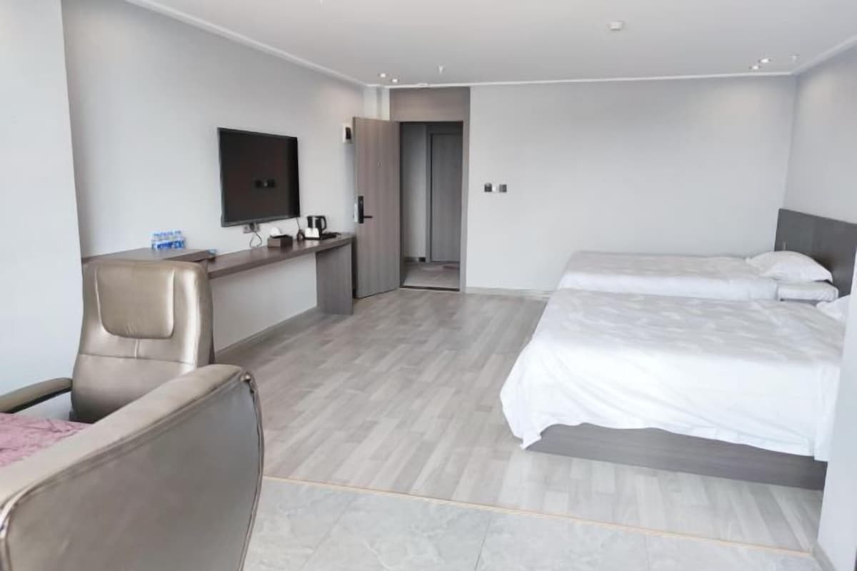 Quarto de hotel moderno com cama, escrivaninha, cadeira e televisão.