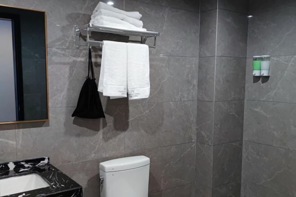 Casa de banho com chão em mármore, sanita branca, lavatório com bancada preta e porta-toalhas com toalhas dobradas.