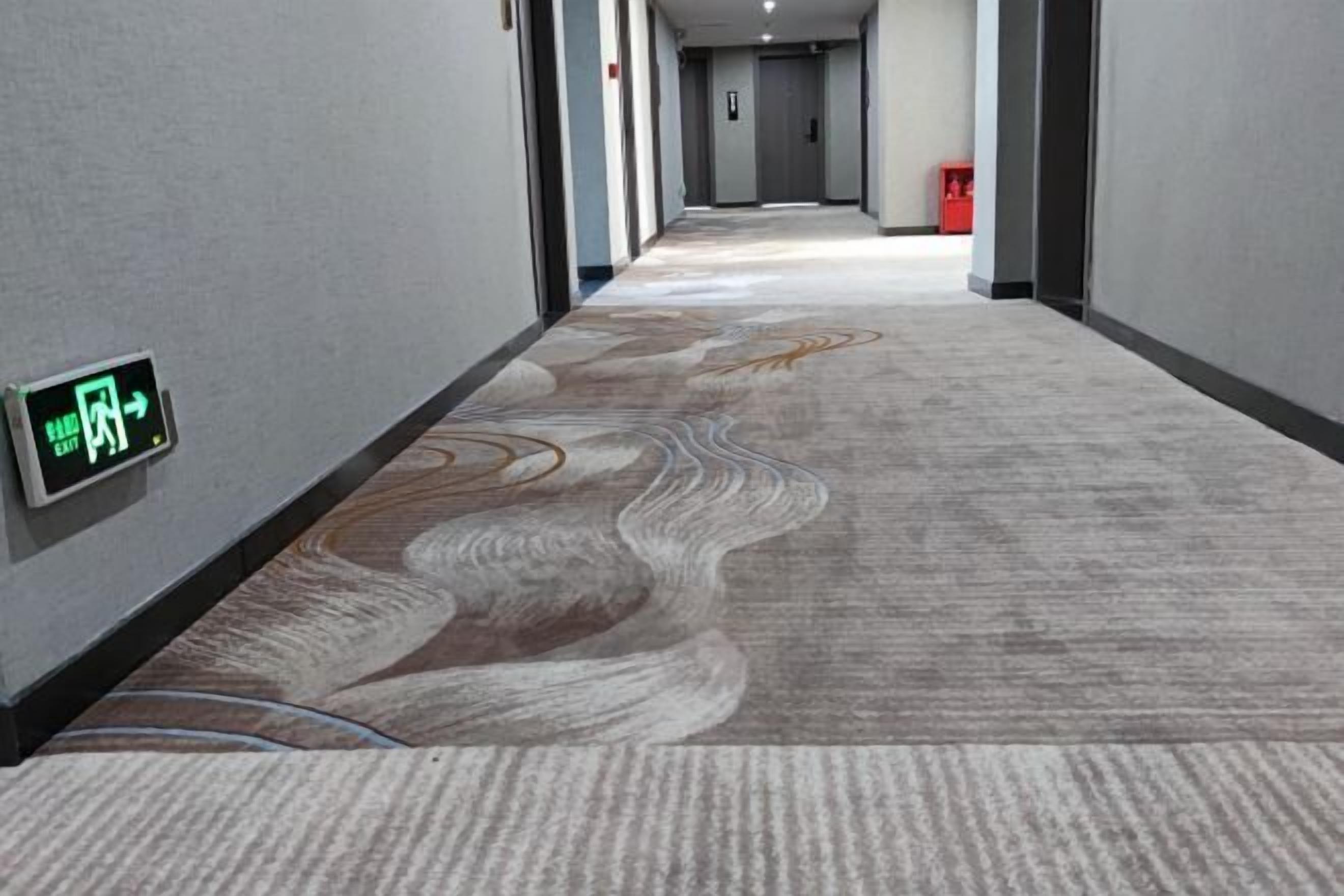A hallway with patterned carpet, a directional sign, and a fire extinguisher.