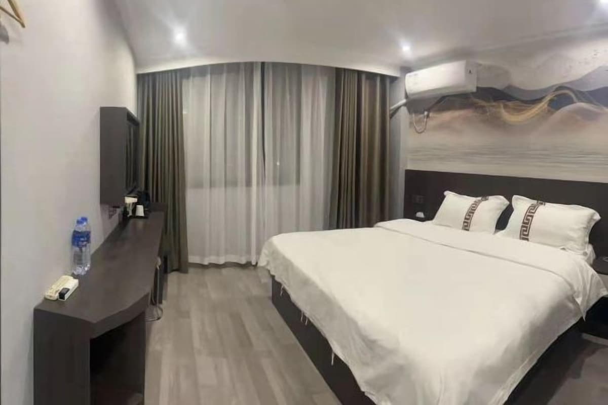 Una habitación de hotel con cama, escritorio, teléfono, una botella de agua y cortina.
