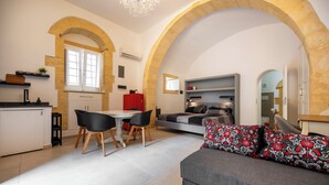 Un interior moderno con zona de comedor, sofá y cama bajo un arco de piedra.