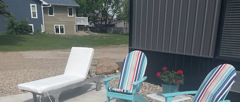 Un patio con dos sillas Adirondack, una silla de lounge y un brasero de metal.