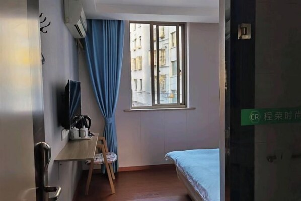 A room with a bed, a desk with a chair, a window with curtains, and a television on the wall.