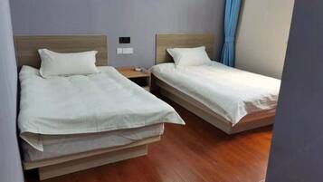Two single beds with wooden headboards, a nightstand, and a blue curtain.