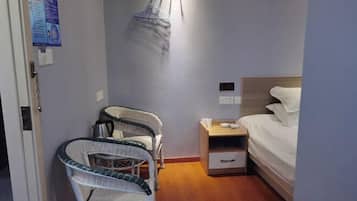 Quarto pequeno com cama, cadeira, mesa de cabeceira e um varal preso à parede.