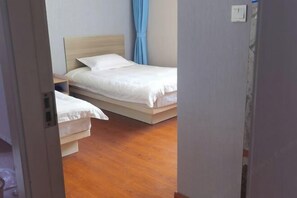 A bedroom with two single beds, a wooden floor, a nightstand, and a blue curtain. - Chengrong Hotel (Shanghai)
