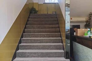 A staircase with a handrail, leading to a landing with a plant and a window. - Chengrong Hotel (Shanghai)