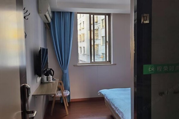 A room with a bed, a desk, a chair, a window with curtains, and a door with a sign. - Chengrong Hotel (Shanghai)
