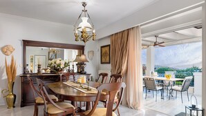 A dining area with a round table, wooden chairs, a chandelier, and a view of the outdoors. - Renko Royal Villa  Luxury villa in Athens Riviera. Private Pool,  garden & BBQ (Lagonisi)