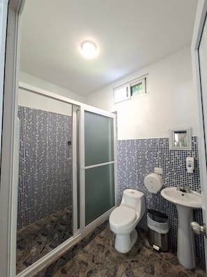 A bathroom with a shower, toilet, sink, and tiled walls. - Hotel Pazifico Monterrico (Taxisco)