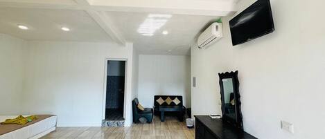Una habitación amplia con una cama, un tocador, un televisor y un equipo de aire acondicionado.