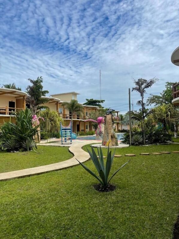 Een hotelbinnenplaats met een pad, palmbomen en een speeltuin.