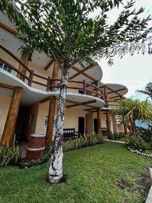 A multi-level building with a central atrium, a tree in the foreground, and a well-maintained lawn.