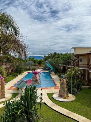 A pool area with a slide, surrounded by greenery and buildings. - Hotel Pazifico Monterrico (Taxisco)