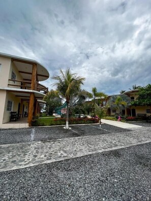 A courtyard with a palm tree, a building with a curved facade, and a paved walkway. - Hotel Pazifico Monterrico (Taxisco)