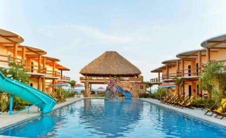 A swimming pool with a slide, lounge chairs, and a thatched-roof structure.. Hotel Pazifico Monterrico