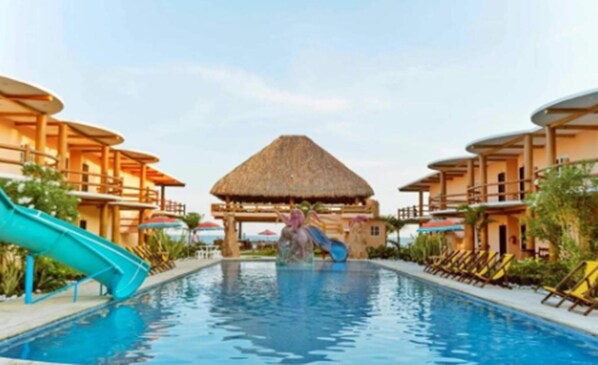 A swimming pool with a slide, lounge chairs, and a thatched-roof structure. - Hotel Pazifico Monterrico (Taxisco)