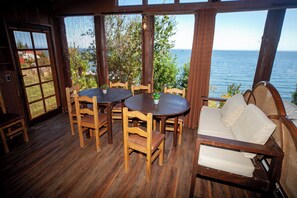 En træterrasse med et rundt bord og stole, en sofa med hynder, og udsigt til havet.