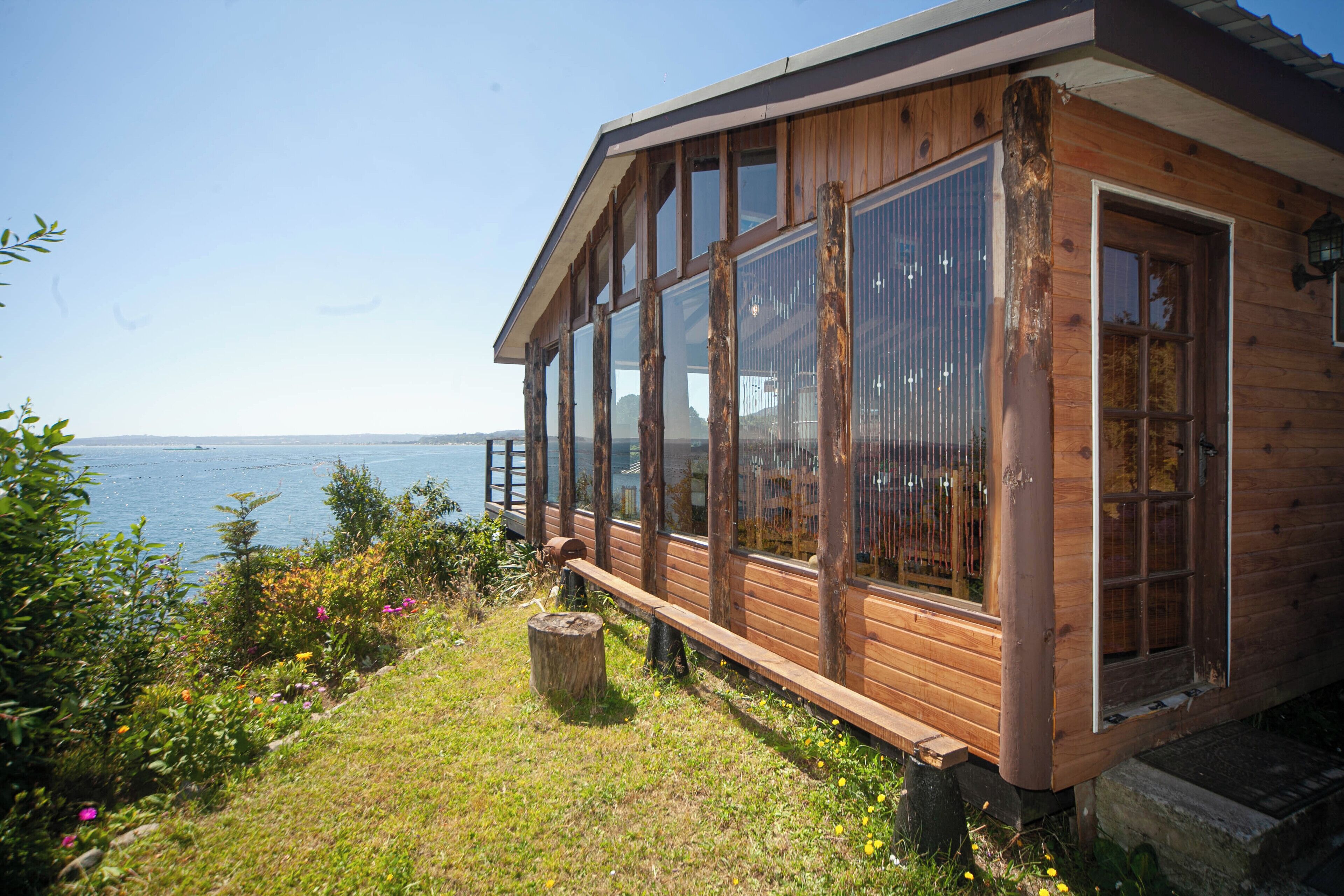 A wooden cabin with large windows overlooking a body of water.