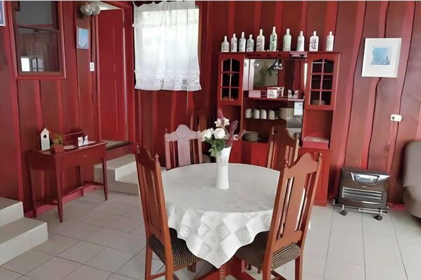 A dining area with a round table, chairs, a vase with flowers, and a red wall with shelves containing bottles. - Lodge Patagonia Carretera Austral (Puerto Montt)