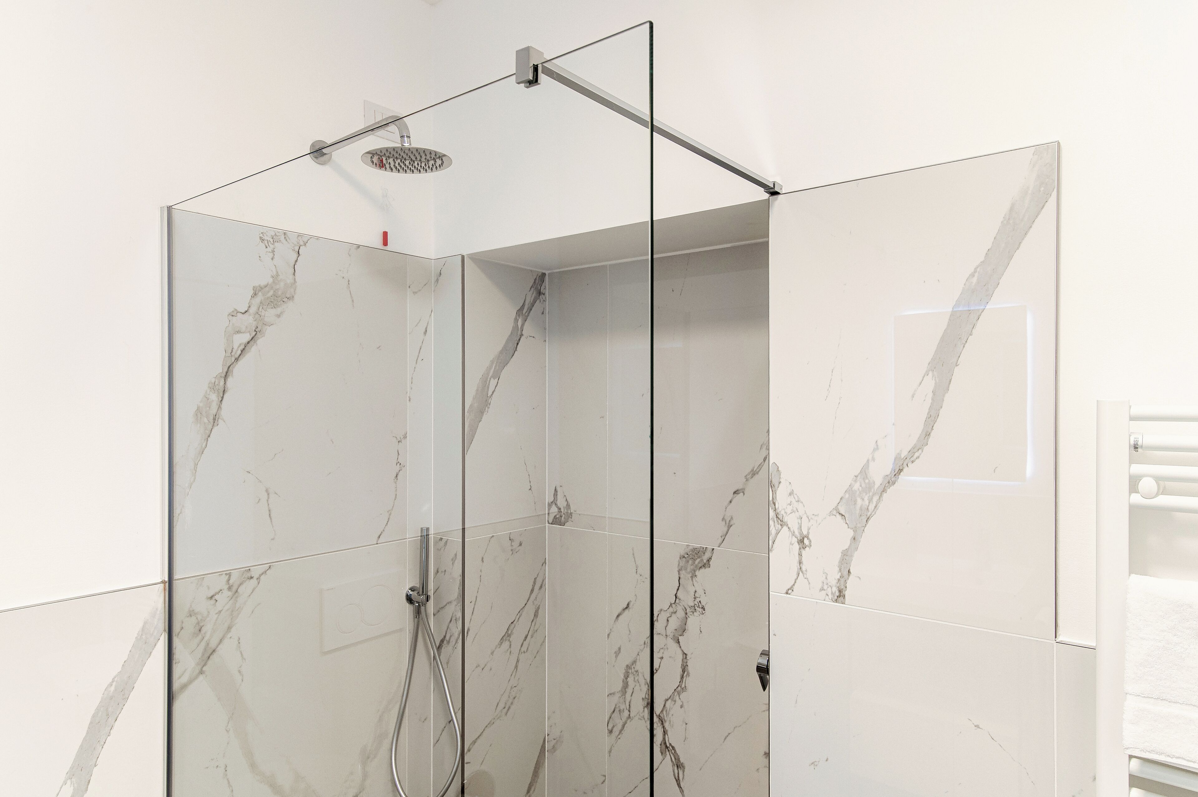 Un box de ducha moderno con azulejos de mármol y puerta de cristal.