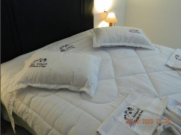 A neatly made bed with white bedding and pillows, each featuring a logo and text. - Estalagem Floradas da Serra  (São Joaquim)